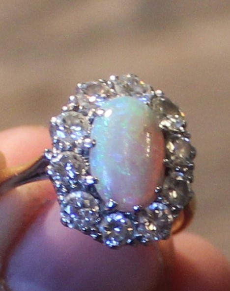 A precious opal and diamond cluster ring, set oval cabochon opal to centre bordered by ten round