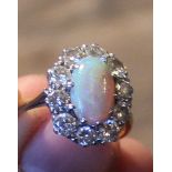 A precious opal and diamond cluster ring, set oval cabochon opal to centre bordered by ten round