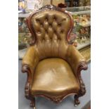 A Victorian style mahogany carved leather upholstered button back nursing armchair on cabriole