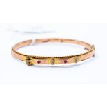 A 9ct rose gold late Victorian early Edwardian bangle set with rubies and seed pearls in the form of