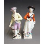 A pair of Berlin figures of a shepherd and shepherdess, she with a lamb and he with a dog at their