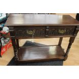 A dark oak two drawer condole table with carved decoration and metal handles to drawers and lower