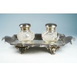 A George V silver inkstand, shaped rectangular with scrolled border plain body with pen insets and