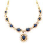 A sapphire and diamond cluster drop pendant necklace, the drop pendant comprising a central oval