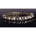 An Edwardian diamond and pearl set bangle, the open work top with fleur-de-lis details set with