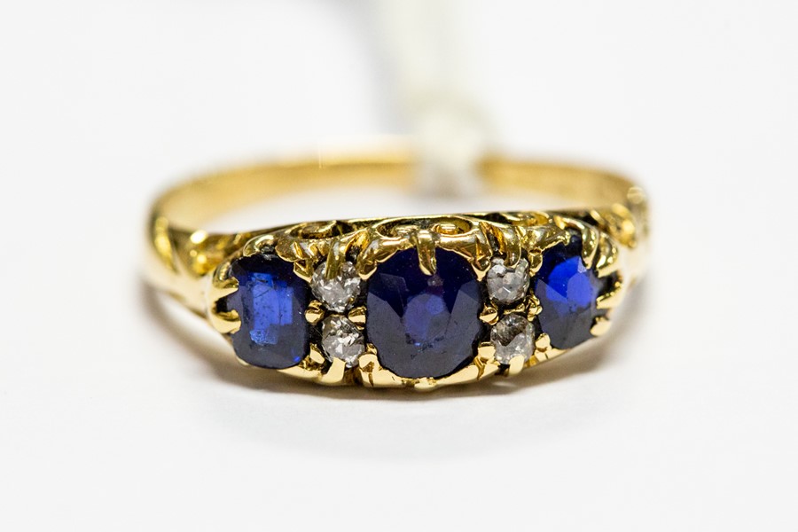 An 18ct gold ring, set with three blue sapphires with diamond set accents, size R, total gross