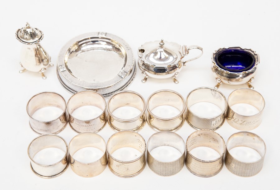 A collection of silver items to include a mustard, pepper and salt set, various napkin rings and a