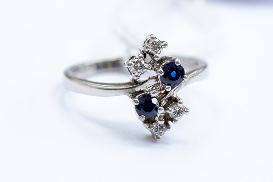 A sapphire and diamond ring, cross over shoulders with round cut sapphire and brilliant cut