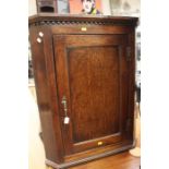 A George III oak wall hanging corner cupboard, stepped cornice above a rectangular panel door,