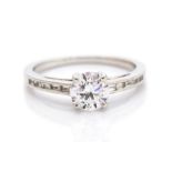 A diamond solitaire white gold ring, diamond set shoulders, the round brilliant cut diamond