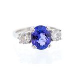 A tanzanite and diamond, platinum three-stone ring, the claw set oval cut tanzanite weighing