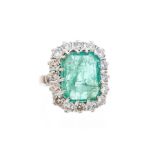 An emerald and diamond cushion shaped cluster 18ct white gold ring, the central emerald-cut