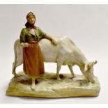 An early Royal Dux figurative group of a cow and dairy maid, seated on a plinth, some damage to