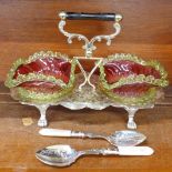 A plated preserve stand with a pair of cranberry and green glass dishes and two serving spoons