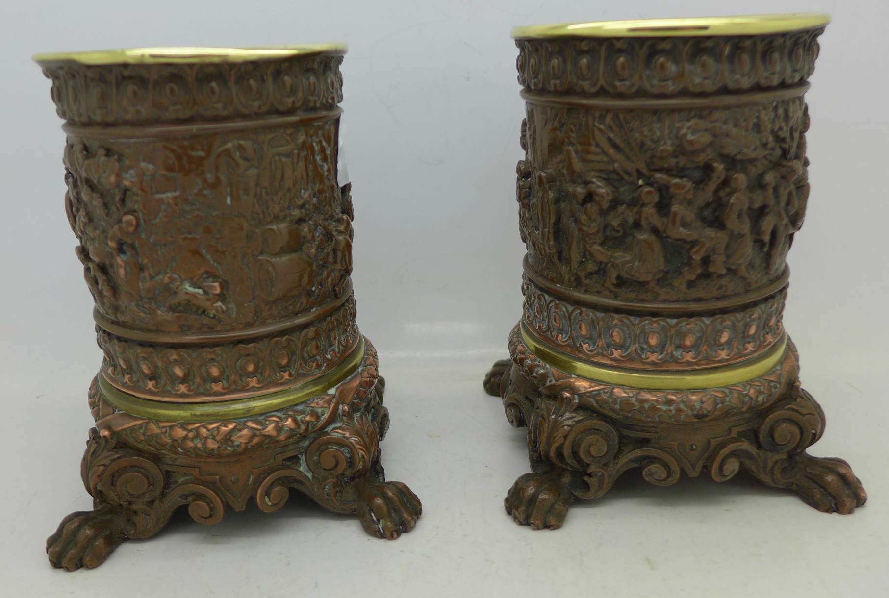 A pair of copper plated and brass lined candle holders with embossed tavern scenes,