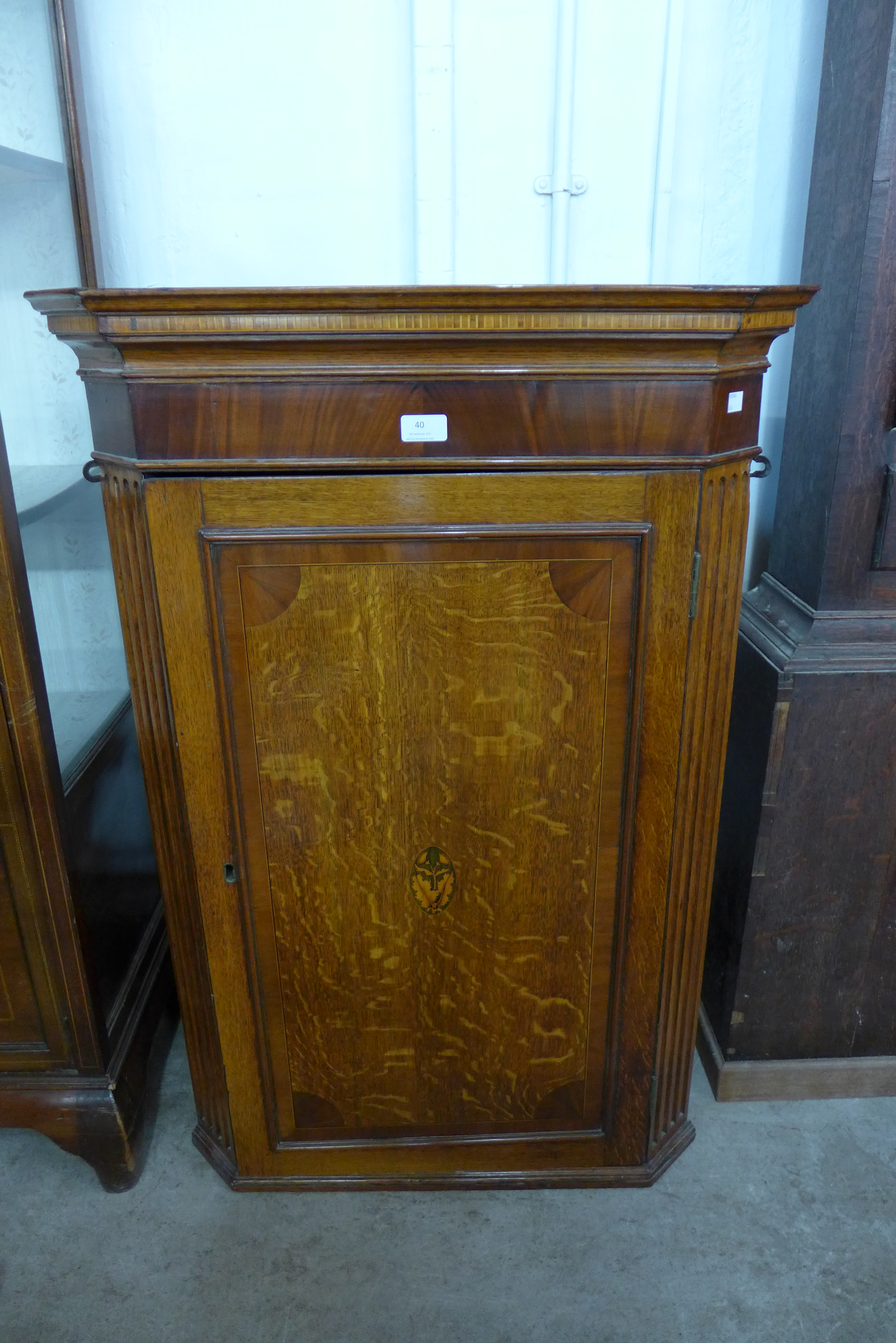 A George III inlaid oak splay front hanging corner cupboard