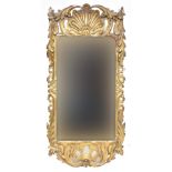A carved giltwood wall mirror, the rectangular plate surrounded by a trailing leaf border surmounted