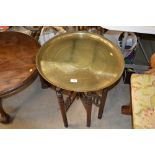 An Eastern brass tray top table raised on folding