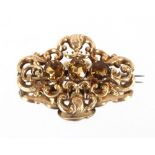 A Victorian yellow metal pierced and scrolled brooch, broad set with three faceted stones