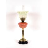 A brass column table oil lamp, having pink opaque glass foliate reservoir and tinted Vaseline