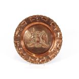 A circular copper tray, having continuous floral border and central crest, 30cm dia.