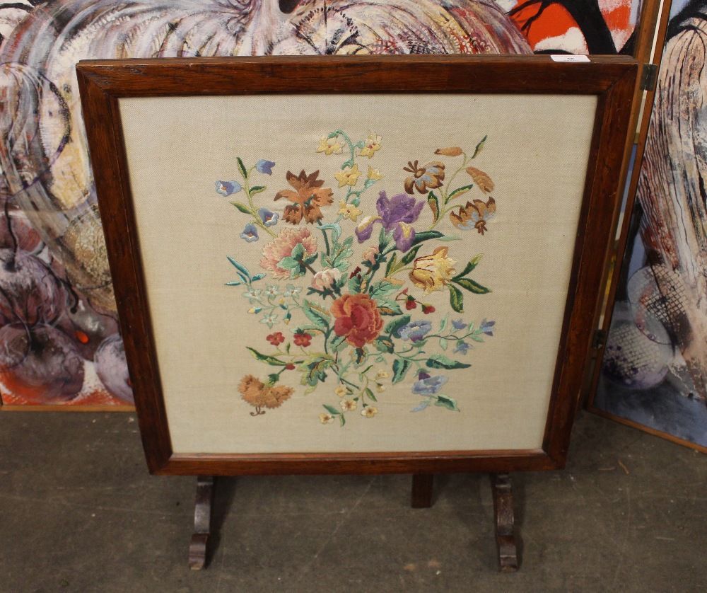 A 1930's oak folding fire screen/occasional table, with floral embroidered panel