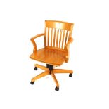 A modern light wood revolving desk chair, having slatted back and solid seat, raised on adjustable