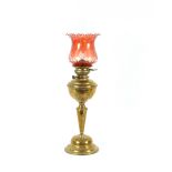 A Victorian brass table oil lamp, with foliate embossed decoration and ruby tinted dimpled shade