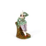 A 19th Century figural decorated spill holder, in the form of a Jester reclining on a tree stump,