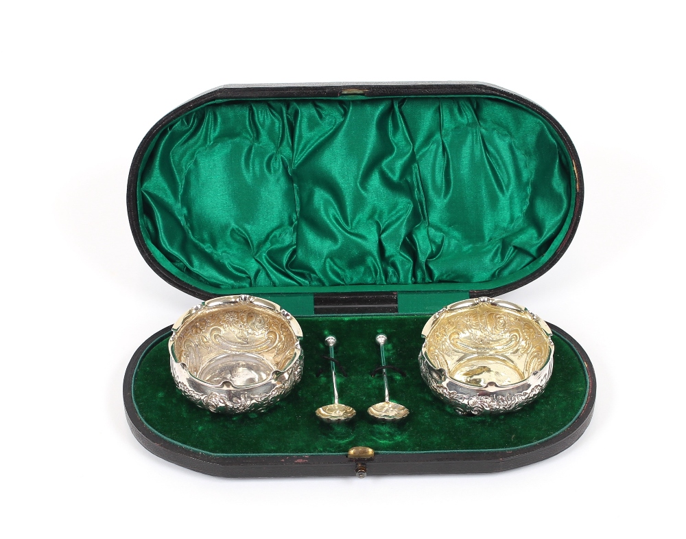 A pair of Victorian silver salts, having floral embossed decoration, shaped borders, raised on