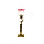 A Duplex brass corinthian column oil lamp, having moulded glass reservoir and ruby tinted shade,