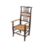 An antique Yorkshire elm spindle back elbow chair, with rush seat raised on rounded tapering