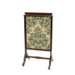 A Victorian mahogany pull-up fire screen, having embroidered panels, raised on scroll supports