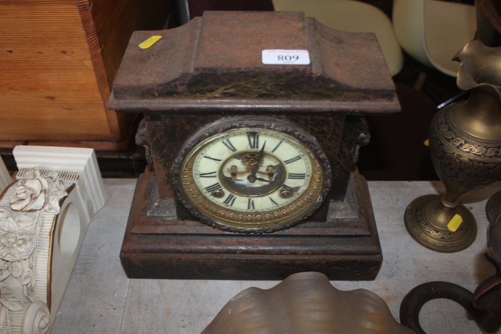 A metal cased two hole mantel clock with mask deco