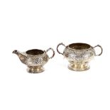 A George III silver cream jug and sucrier, having rich foliate embossed decoration and cartouche