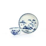 An English porcelain blue and white tea bowl and saucer, decorated with a river scene with flowers