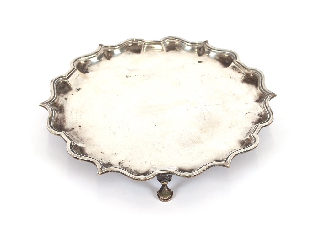 A silver salver, by Elkington & Co., having pie crust border, raised on three hoof feet,