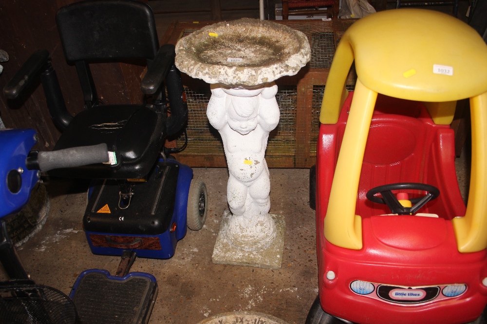 A concrete bird bath raised on figural base