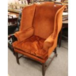 A Georgian style mahogany winged back armchair, upholstered in rust coloured dralon, raised on