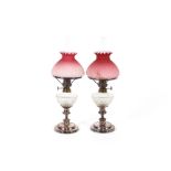 A pair of peg oil lamps, having electro plated bases, cut glass reservoirs and pink opaque glass