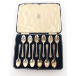 A cased set of twelve silver teaspoons, with stylised decoration to the handles, retailed by