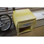 A yellow painted bedside table with single draw