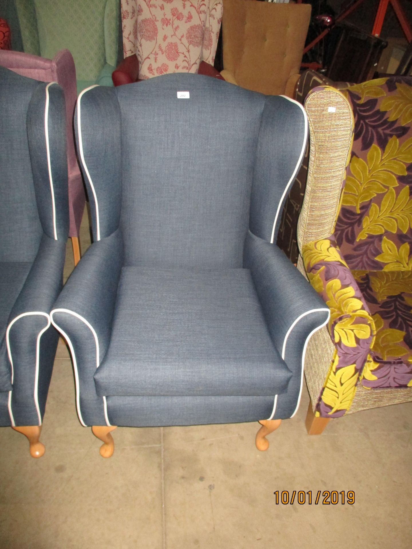 A Bretton blue upholstered wing back armchair with white vinyl trim on light wood feet