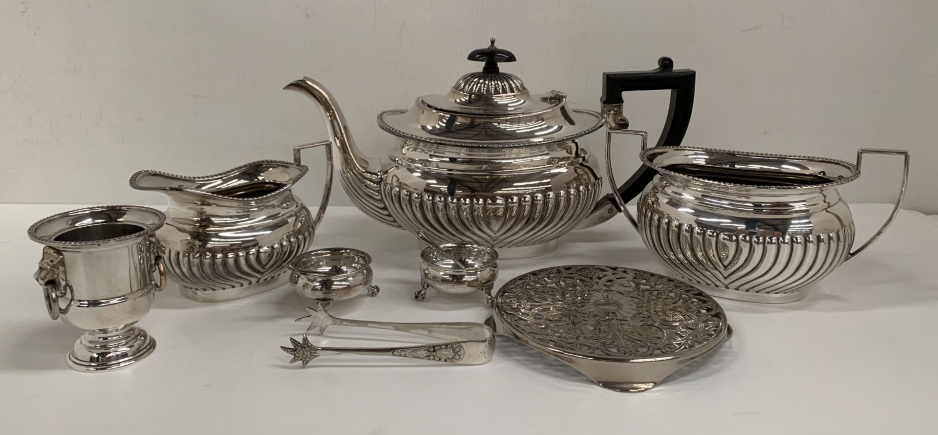 A plated three piece tea service, a plated stand, two plated salts and spoons,