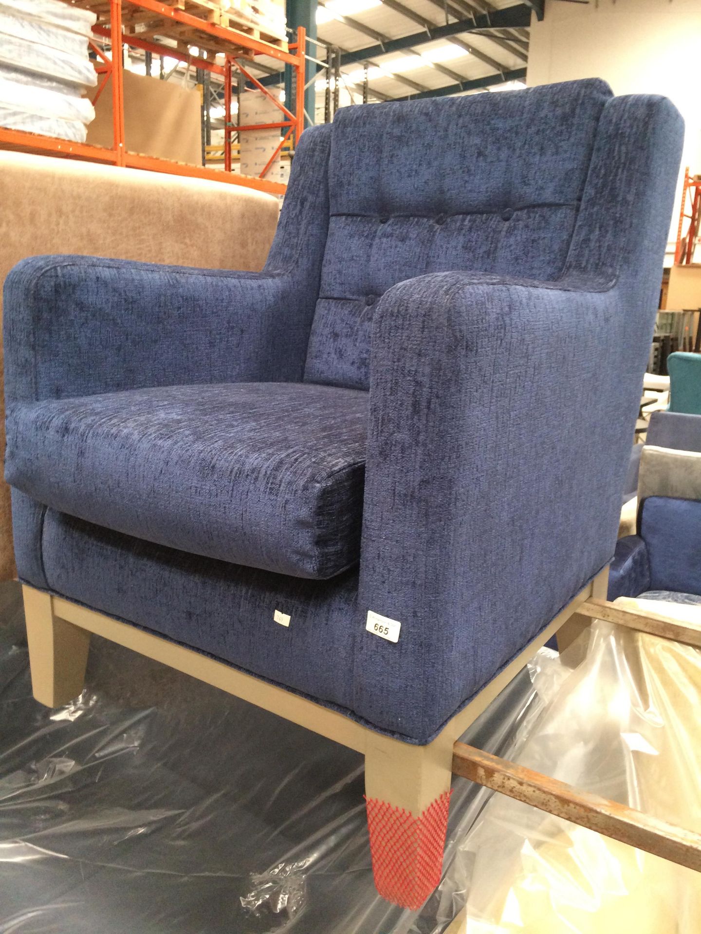 A deep blue upholstered button backed armchair on grey wooden feet
