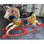 A painted fibre glass rocking horse in the style of a fairground horse on red painted wood rockers