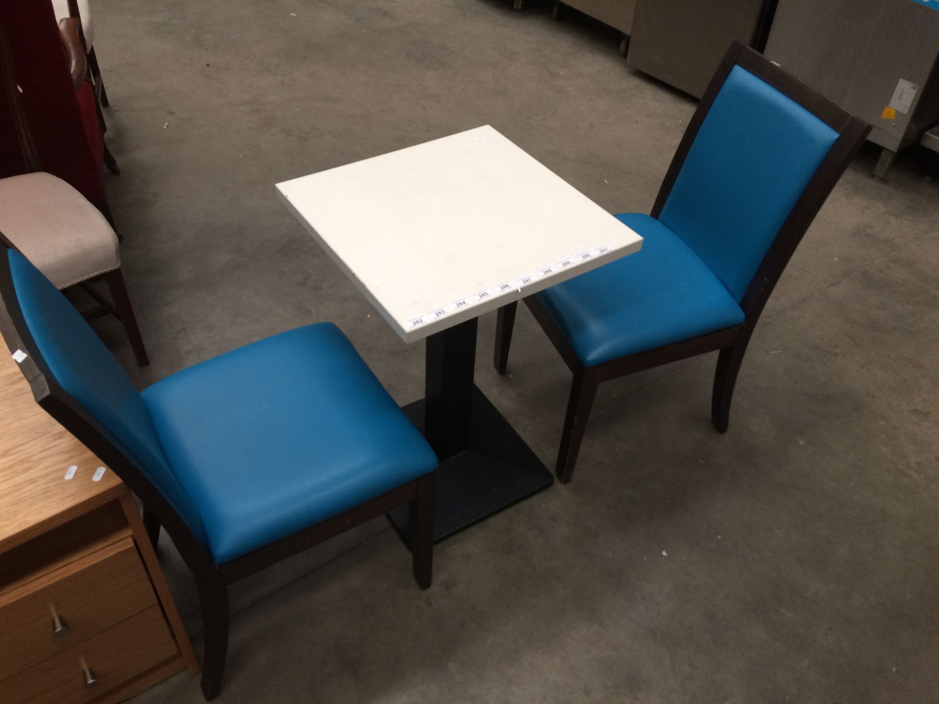 A white square cafe table 50 x 50cm on black metal base complete with 2 x blue vinyl upholstered