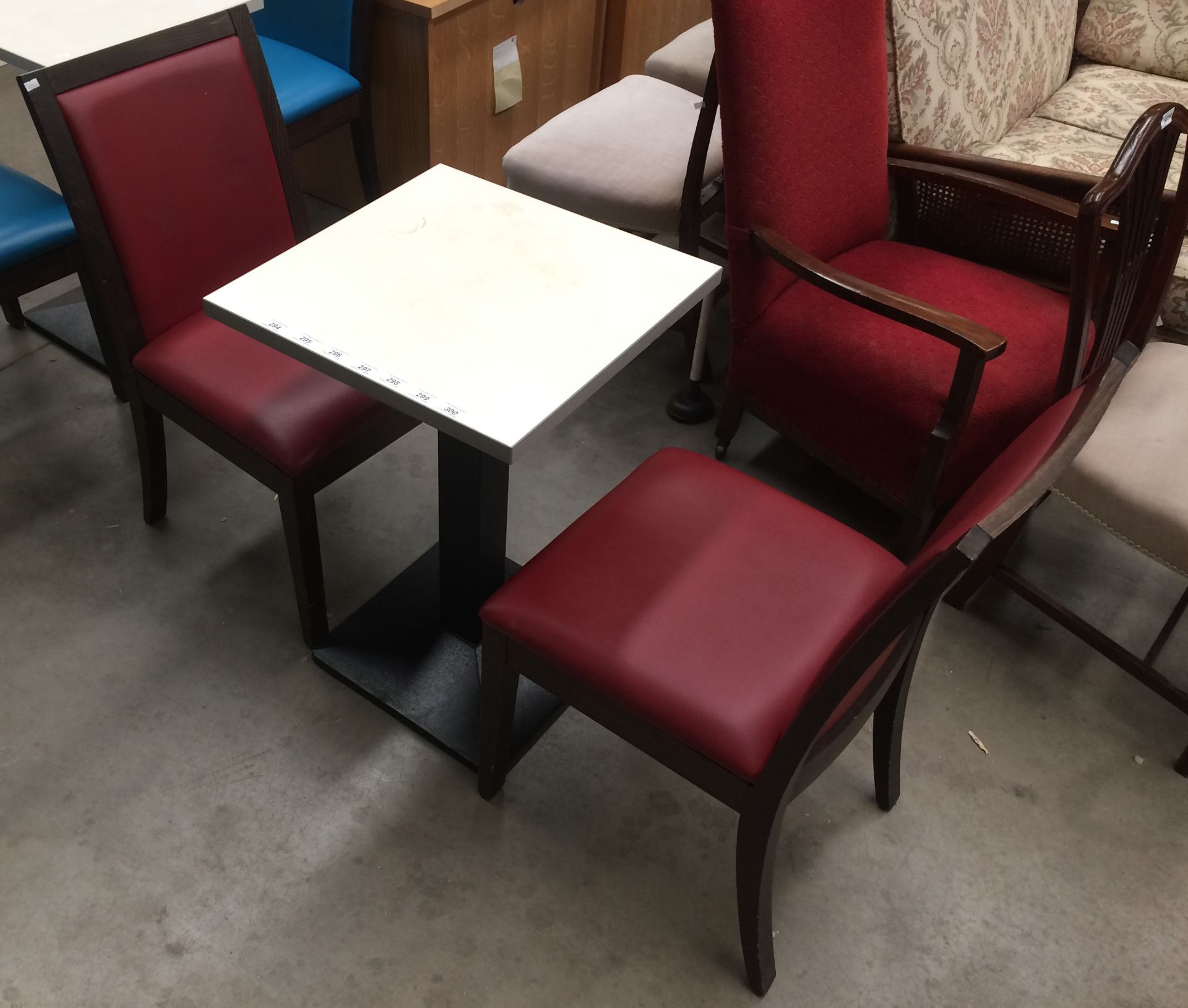 A white square cafe table 50 x 50cm on black metal base complete with 2 red vinyl upholstered