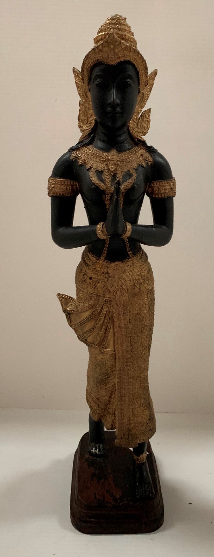 A gilt and black coloured metal figure of an oriental goddess at prayer on wood base