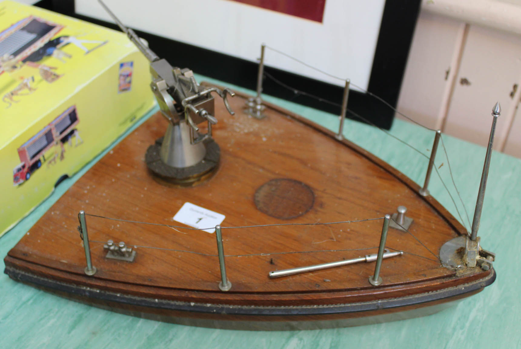A mahogany model boat prow to which is attached a steel deck gun with movable parts